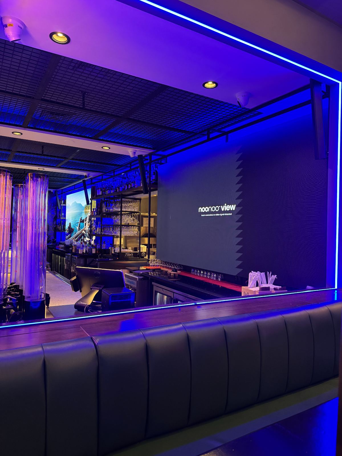 A bar lit in blue and violet with screens along the wall