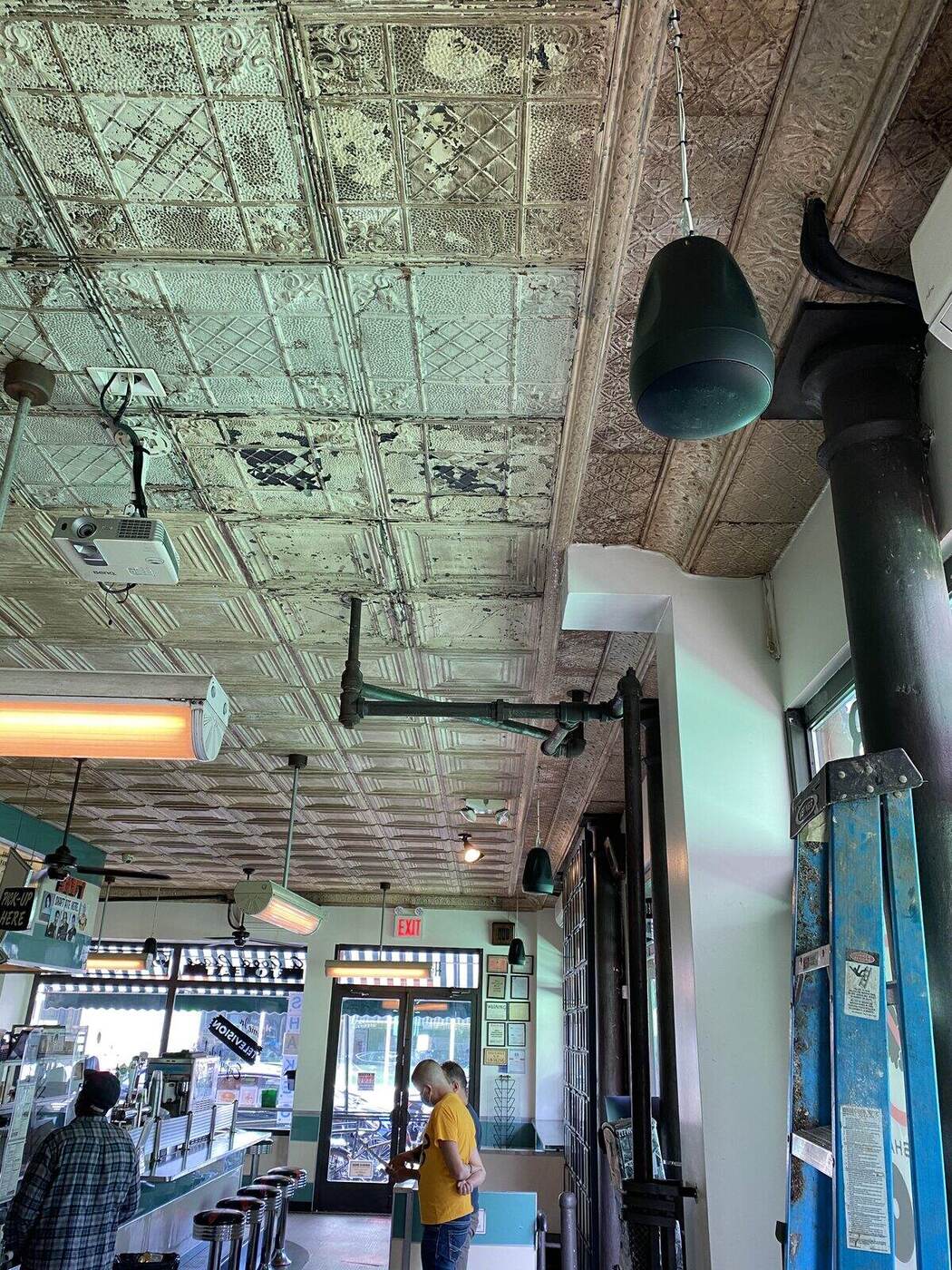 Pendant speakers and heaters hung from a pressed-tin ceiling over a counter